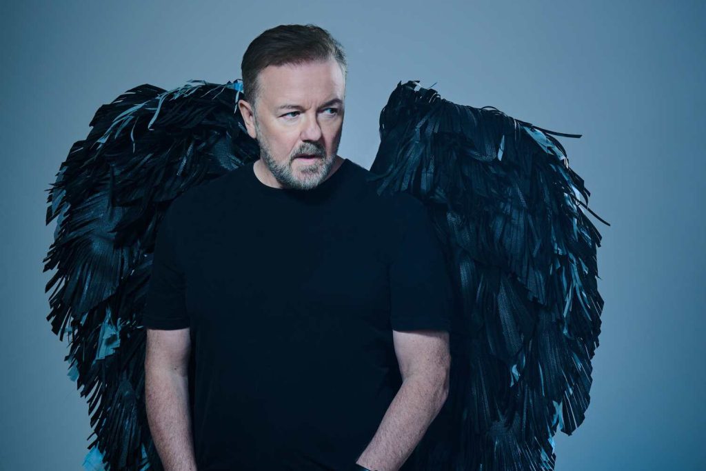 Ricky Gervais uppträder snart i Stockholm. På den här pressbilden står han med svart T-shirt och har svarta vingar på ryggen.